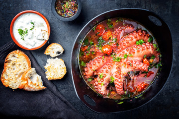 Traditional Greek octopus braised cooked with tomatoes and herbs in ouzo sauce with tzatziki as top view in a cast-iron saucepan