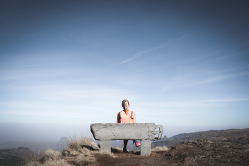 Young woman sitting on a bench at a beautiful viewpoint