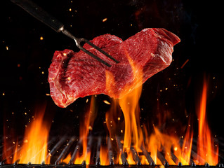 Flying raw beef steak above burning grill grid