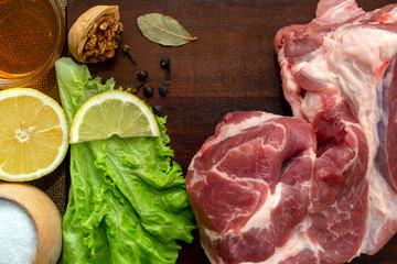 A slice of raw pork meat on a wooden cutting board. Leaf lettuce, seasonings and a slice of lemon. Rustic style, top view.