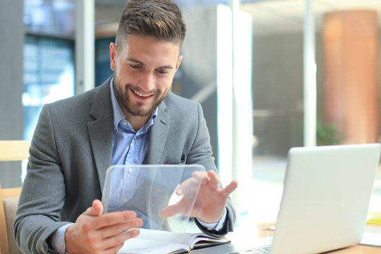 Businessman working in office with transparent tablet and laptop. - Powered by Adobe