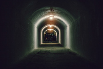 Crowd of silhouettes of people in end of dark creepy underground tunnel or corridor, copy space