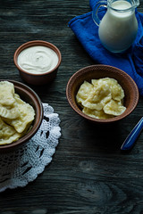 Dumplings with potatoes and cabbage. Sour cream, milk and greens. Traditional dish of Ukraine. Dark wooden background.
