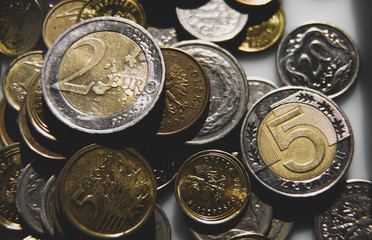 Two euro coin lying over stack of polish zloty coins. Coins stacked in different positions. Closeup, macro shot. Colors ma.