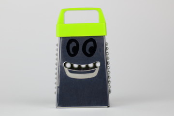 Stainless steel grater with painted eyes for vegetables with a green pen.