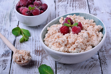 Cottage cheese topped with raspberries in a bowl on white wooden table
