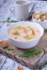 Cream soup with croutons, green onion and cheese in a white bowl