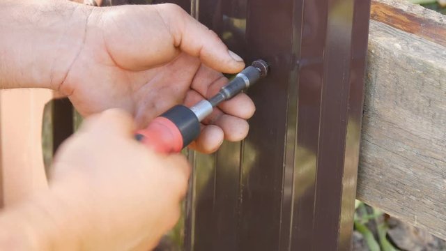 Male hands fix the fence with special screws and a manual screwdriver