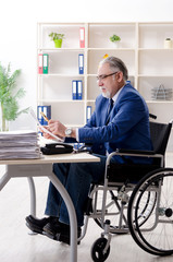 Aged employee in wheelchair working in the office 