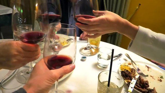 four hands holding red wine and doing cheers to celebrate in a restaurant.