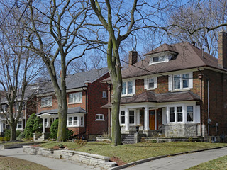 Row of large old  detached brick houses with mature trees in the front yard