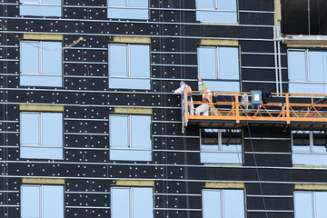 construction winch with workers on a concrete wall of a high-rise building with brick walls and...