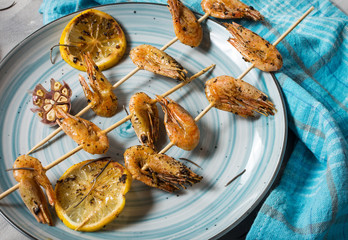 Grilled shrimp skewers with herbs, garlic and lemon on concrete background. Seafood