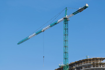Fototapeta na wymiar high-rise construction crane with a long arrow of yellow color against the blue sky over a new multi-storey building of concrete and brick under construction