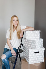 Young woman moving in her new house and doing a home makeover, she is sitting on the ladder with many cardboard boxes around