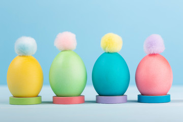 Dyed bright Easter eggs in stands with colorful pompons on a blue background.