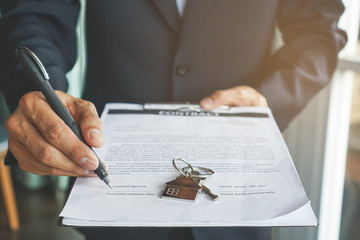 close-up view hands of businessman signing leasing home documents and have a apartment keys on...