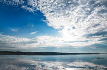 Fototapeta premium Morning dawn on the river Bank. Reflection of the blue sky in the river. Bright reflection of the sun and rays.