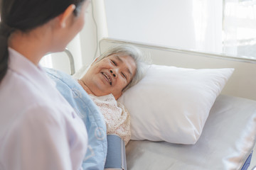 Fototapeta premium Asian elderly look at her caregiver. nurse putting blanket on senior woman on the bed in the nursing home.