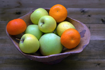 fresh green apples and tangerines in a vase on a wooden background