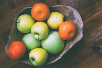 fresh green apples and tangerines in a vase on a wooden background