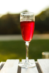 wineglass with red champagne stand on wooden table at green summer park background