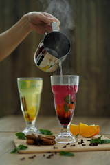 Pouring hot steaming water from steel pot in glass with vitamin drink. winter hot seasonal drinks