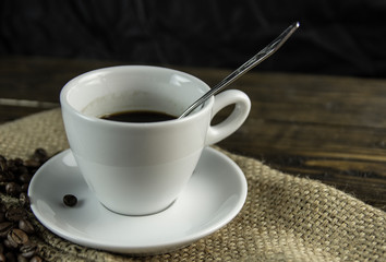 Cup of coffee and coffee beans on a rough wooden background.