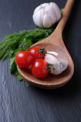 Red Tomatoes garlic and greens in a wooden spoon on a stone background.