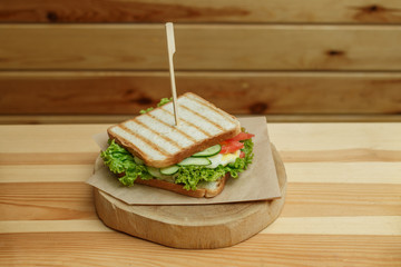 juicy sandwich with bacon, fresh vegetables, green salad and dark lines after grill on wooden plate