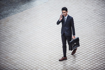 Young executive businessman using a mobile phone in the business district with skyscrapers buildings background