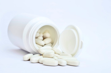 White oval pills spilled out of the white bottle on a white background.