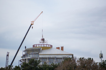 Bottom view amazing view of building under construction with dome and crane with arrow on background dense white clouds