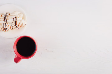 A meringue cupcake and a cup of coffee on a white wooden table.