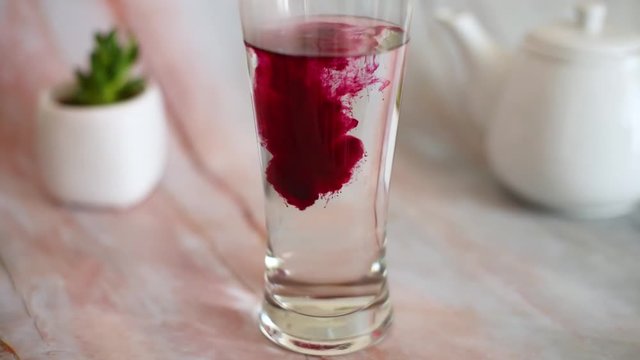 Pink food coloring dissolves in a glass of water close up. Preparation for painting eggs. Shot at 60fps, HD format