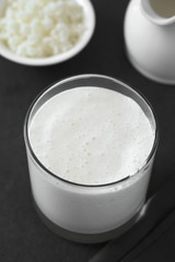 Fresh homemade kefir drink in glass, kefir grains and milk in the back, photographed with natural light (Selective Focus, Focus one third into the kefir drink) (Digitally Altered: Desaturated Image)