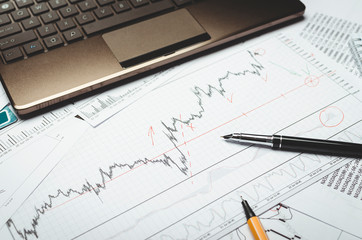 Analysis of financial charts on paper, pen and laptop