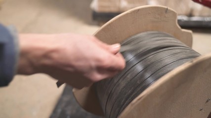 A close-up of a worker taking plastic wrapping rope from a spool to pack the briquettes