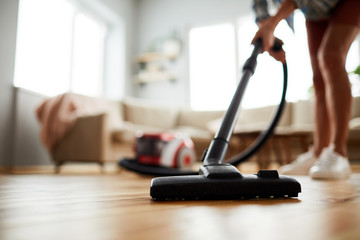 Close-up of unrecognizable woman using modern powerful hoover while vacuuming floor at home - obrazy, fototapety, plakaty