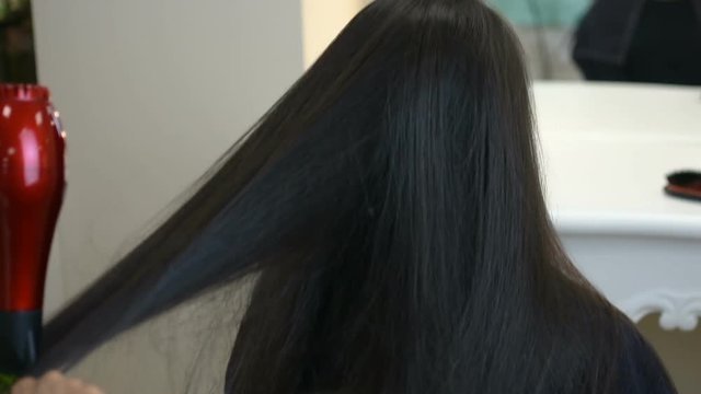 Young girl gets her long black hair styled by professional hairdresser 