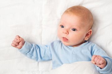Portrait of a cute baby lying down on a bed. Baby on white cloth lying on his back