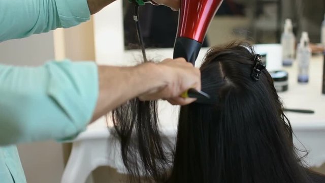 Hairdresser making long black hair looks perfect in his hands