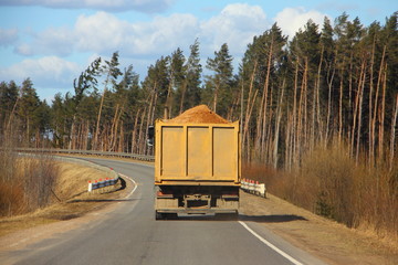Transportation, logistics - dump truck carries sand on asphalt road on the forest background © Ilya