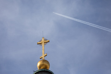 A plane flies high in a cloudless blue sky over a church steeple. fear of superstition