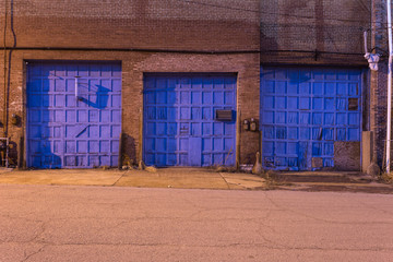 Three blue doors on a vintage red brick industrial warehouse in a depressed urban area