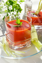 .Tomato juice is poured into a transparent glass with parsley and herring, on a white background, illuminated by sunlight.