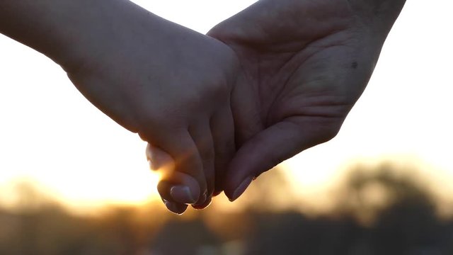 Close the hands of mother and child. Hold hands at sunset. Give a hand to a friend. The sun's rays shine through their fingers. Love, Happiness and Friendship. Hands close up.