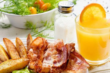 Homemade breakfast with potatoes with crispy bacon, tender egg and a glass of fresh juice on a white table background.