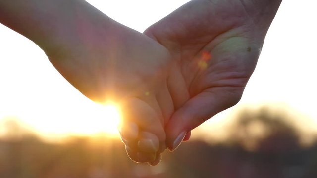 Close the hands of mother and child. Hold hands at sunset. Give a hand to a friend. The sun's rays shine through their fingers. Love, Happiness and Friendship. Hands close up.