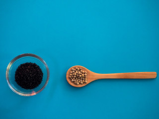 Crystal bowl with common marine salt and a wooden spoon with white peppercorns on a blue background